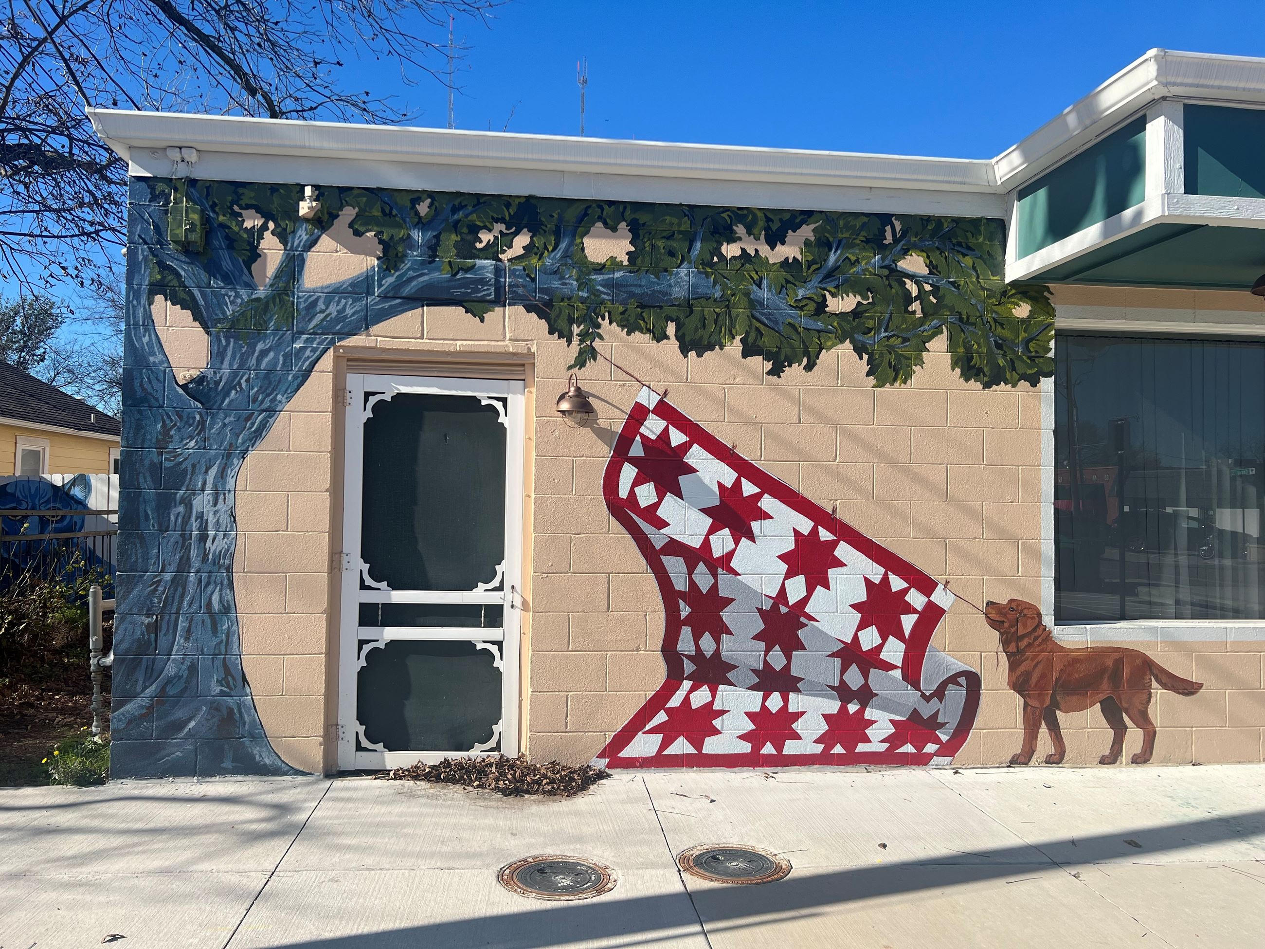 Mural of a yellow dog pulling a red and white checkered quilt down from a tree.
